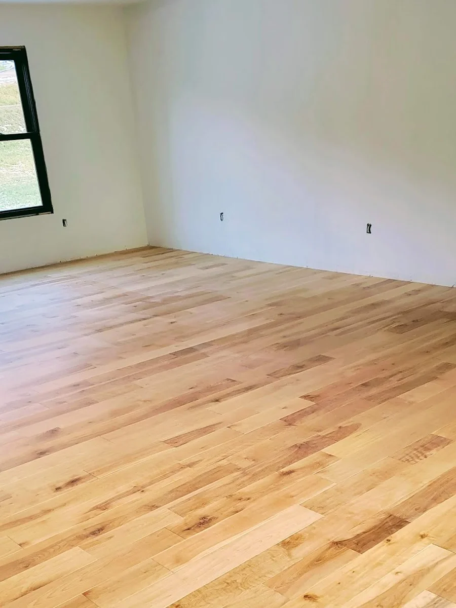 Freshly installed hickory-look hardwood flooring in a sunlit, empty Hudson Valley living room